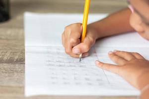 een klein meisje gebruikt een geel potlood dat in een notitieboekje schrijft foto