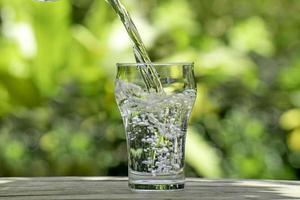 giet water uit een plastic fles in een glas. de achtergrond van de planten in de tuin. zachte focus. foto