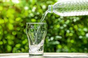 giet water uit een plastic fles in een glas. de achtergrond van de planten in de tuin. zachte focus. foto