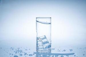 ijsblokje viel in het glas water. water spatte uit het heldere glas. fris concept foto