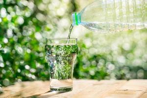 giet water uit een plastic fles in een glas. de achtergrond van de planten in de tuin. zachte focus. foto