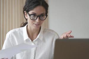 zelfverzekerde vrouw met een bril die aan het bureau zit, werkt thuis op de computer foto