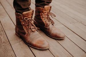 bovenaanzicht van mans schoenen op houten vloer of oppervlak. oud schoeisel. onherkenbaar mens. leren ruige bruine laarzen met veters foto