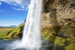 uitzicht op seljalandsfoss met regenboog die uit de berg stroomt tegen bewolkte hemel foto