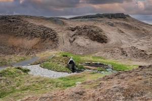 schilderachtig turfhuis en warmwaterbron op de berg in hrunalaug tegen bewolkte hemel foto