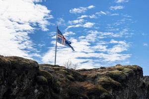 IJslandse vlag zwaaien op rotsachtige klif tegen blauwe bewolkte hemel foto