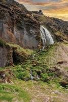 prachtige gljufrabui-waterval die van de berg stroomt tegen de bewolkte hemel bij zonsondergang foto