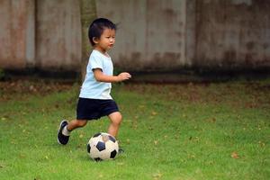 Aziatische jongen voetballen in het park. kind dribbelende bal in grasveld. foto