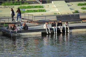 Vilnius, Litouwen. 06 juni 2022 - tienervrienden zitten op een houten pier boven de rivier, praten en hebben plezier foto