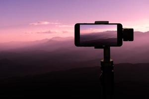 reiziger die smartphone op statief gebruikt en een foto maakt bij zonsondergang op de natuurlijke achtergrond van de bergen.