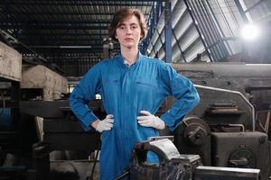 portret van een jonge blanke vrouwelijke industriearbeider in veiligheidsuniform, kijkend naar camera en akimbo en drukt plechtig vertrouwen uit in een mechanische fabriek. beroep ingenieur. foto