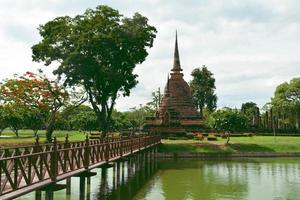 de houten brugweg naar de belangrijkste laterietpagode in het historische park in sukhothai. foto