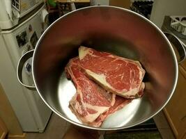 hand met biefstuk in metalen pot in de keuken foto