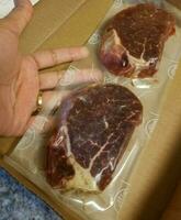 hand met rauwe steaks in een plastic zak en kartonnen doos foto