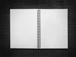 leeg spiraalvormig notitieboekje op een zwarte leerachtergrond foto