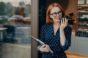 vrouwelijke freelancer staat buiten met mobiele telefoon en gebruikt spraakherkenningssysteem op smartphone foto