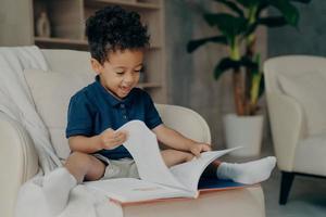 gelukkig gemengd ras klein kind met schattig krullend haar leesboek thuis foto