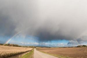 panorama van het veld langs de weg met een regenboog en stormachtige lucht foto