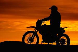 zwart silhouet van fietser met motobike op oranje zonsonderganghemelachtergrond foto