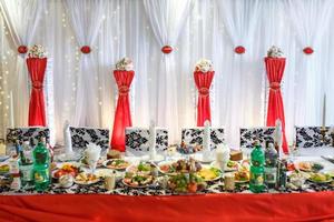 versierde bruiloftstafel in de feestzaal. tafel voor pasgetrouwden versierd met rode linten foto