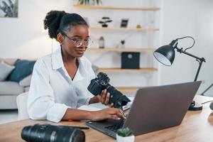 camera houden. jonge Afro-Amerikaanse vrouw in wit overhemd is thuis foto