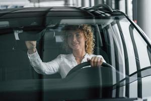 op de bestuurdersstoel zitten. vrouw met krullend blond haar is in autosalon foto