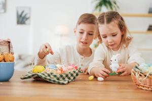 bij de tafel zitten. gelukkige kleine zus en broer die samen paasvakantie vieren foto