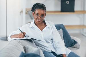 huiskamer. jonge Afro-Amerikaanse vrouw in wit overhemd is thuis foto