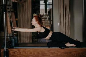 roodharige vrouw doet stretching-routine op cadillac-machine of trapeze-tafel foto