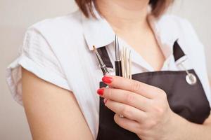 vrouw die een schort draagt met borstels en stokken voor manicure. accessoires voor nagelverzorging en het aanbrengen van nagellak. handen schoonheidsverzorging in salon. foto