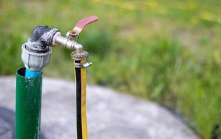 sanitair, waterpomp uit een put. een buitenwaterkraan met daaraan een gele tuinslang. irrigatie water pompsysteem voor landbouw. slang in de tuin voor het drenken, zonnige zomerdag. foto