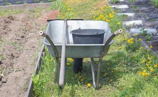 grijze metalen tuinkruiwagen met twee handvatten en één wiel. de kruiwagen staat in de tuin of tuin. tuinman kruiwagen in de achtertuin. tuin schoonmaken. foto