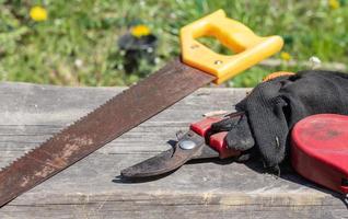 een oude roestige handzaag met een plastic handvat voor houten zaagplanken, multiplex en andere materialen. zaag, tuinschaar met handschoenen. tuingereedschap op een zonnige dag in de tuin. foto