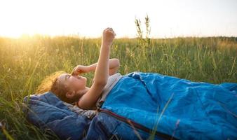 het meisje is ontevreden over het krabben van muggenbeten, kind slaapt in een slaapzak op het gras tijdens een kampeertrip. milieuvriendelijke openluchtrecreatie, zomertijd. slaapstoornissen, afstotend. foto