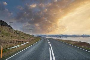 afnemende snelweg te midden van zee en berg tegen bewolkte hemel tijdens zonsondergang foto