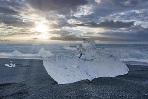 close-up van ijsberg op mooi zwart zandstrand tegen dramatische hemel bij zonsondergang foto