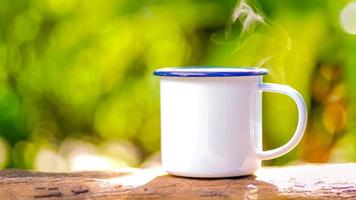 witte emaille koffiemok op de oude houten tafel groene bos bokeh achtergrond foto