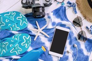 vrijetijdskleding voor dames met accessoires en een smartphone met leeg scherm op een witte houten achtergrond, zomerconcept foto