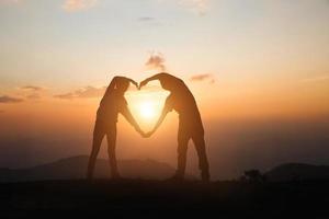 een vrouw en een man maken een hart bij zonsopgang op de berg. god is liefde concept hartvorm berg reizen manifestatie van liefde liefde en gevoelens foto
