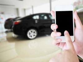 vrouwenhanden die mobiele telefoon met vage achtergrond van nieuwe auto's houden foto