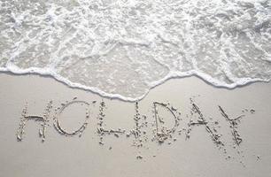 het woord vakantie in hoofdletters in het zand geschreven. foto