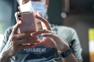 thaise man die het medische masker draagt met zijn mobiele telefoon en nieuws leest over de situatie met de coronaviruspandemie in de coffeeshop. dagelijks leven na covid-19. nieuw normaal levensstijlconcept. foto