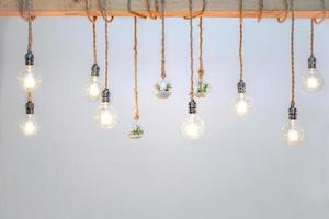 gedecoreerde gezellige lampen steken in het touw en kleine kleine boom met kleine witte rots in het glas van de bal hangen aan grote houten log voor witte achtergrond. foto