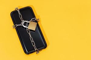 telefoon veiligheidsconcept. smartphone vergrendeld met ketting en hangslot op gele achtergrond. mobiele beveiliging en gegevensprivacy foto