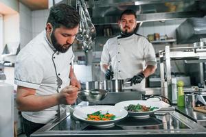twee mannen maken salade. professionele chef-kok die voedsel in de keuken bereidt foto
