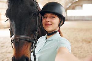 mooie selfie maken. een jonge vrouw in jockeykleding bereidt zich voor op een ritje met een paard op een stal foto