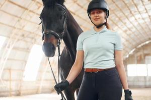 in beschermende hoed. een jonge vrouw in jockeykleding bereidt zich voor op een ritje met een paard op een stal foto