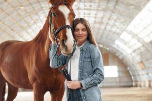 glimlachen en genieten. jonge vrouw in spijkerbroek is met paard op stal foto