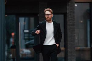 in tijdnood komen. stijlvolle man met baard en bril is buiten in de buurt van gebouw foto