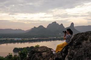 Aziatische fotograaf die tijdens het reizen foto's maakt van zonsondergang over meer en berg foto